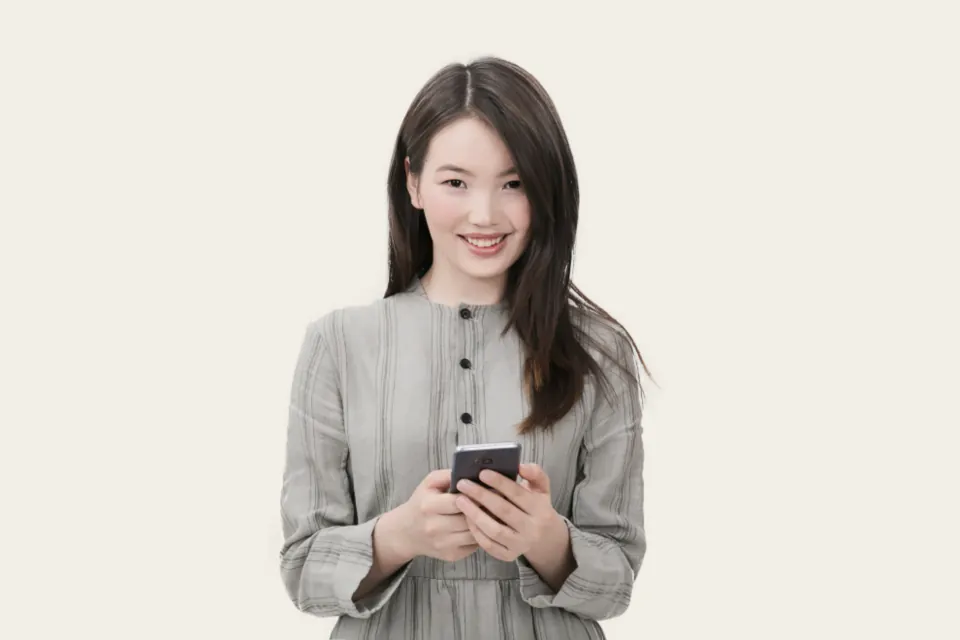 A smiling woman holds a smartphone in both hands.